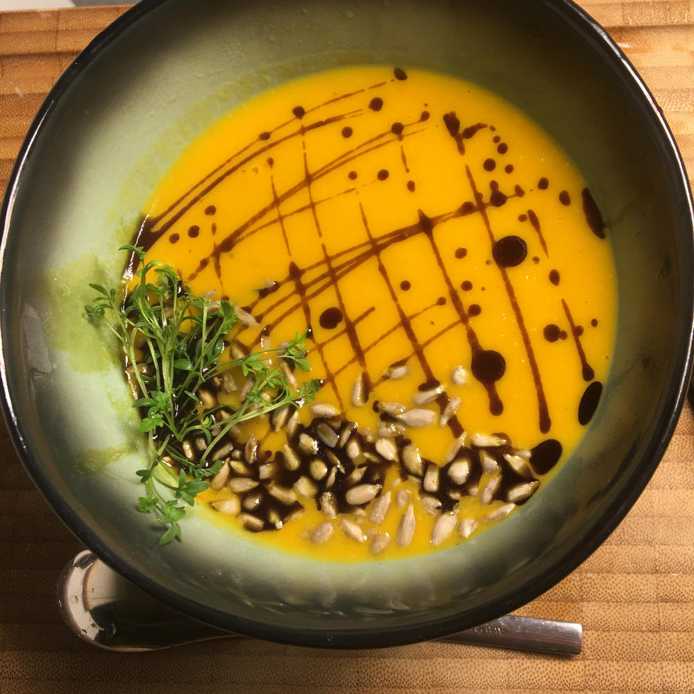 A bowl of orange soup decorated with pumpkin seed oil, sunflower seeds and cress