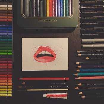 Lips painted with watercolor, a lot of different pens around the postcard sized image