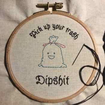 Embroidery of a cute little trash bag with a smily face and text reading 'Pick up your trash Dipshit'